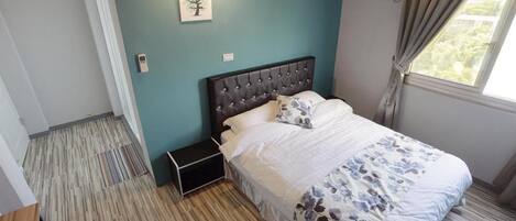A bedroom with a bed, a bedside table, a wall-mounted air conditioner, and a window with curtains.