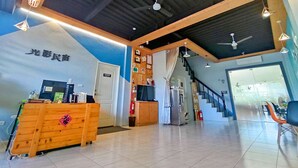A modern hotel lobby with a reception desk, wooden accents, a staircase, and a view of the outside. - Light Shadow (Budai)