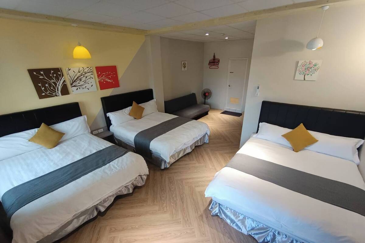 Ein Hotelzimmer mit drei Betten, Holzboden und Wandbildern.
