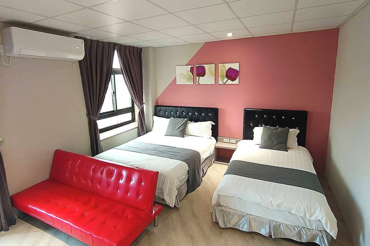 Ein Hotelzimmer mit zwei Betten, einem roten Sofa und einem Fenster mit Vorhängen.