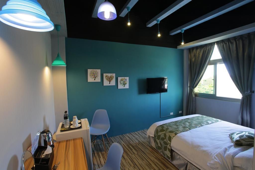 A hotel room with a bed, a desk with a chair, a television, and artwork on the wall.