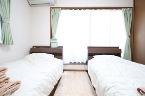 Ein Zimmer mit zwei Betten, Holzboden, einem Vorhangfenster und einer Wandklimaanlage.
