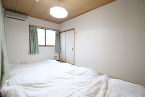 A bedroom with a large bed, a window with curtains, a wooden ceiling, and a door with a mirror.