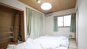 A hotel room with a wooden ceiling, a bed with white bedding, a wardrobe, and a window with green curtains.