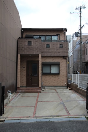 A two-story building with a brown door and windows, a concrete sidewalk, and a metal fence.