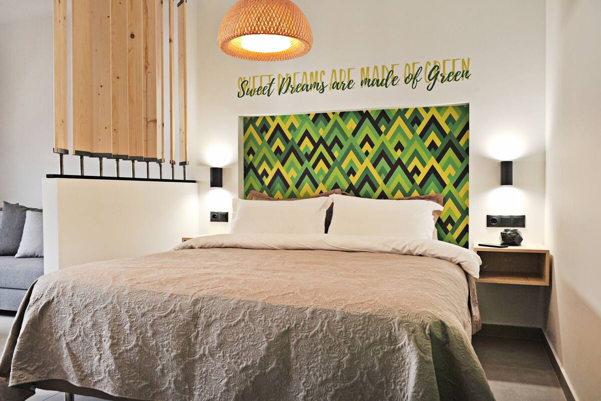 A modern hotel room with a bed, a wall-mounted lamp, and a decorative wall with a geometric pattern.