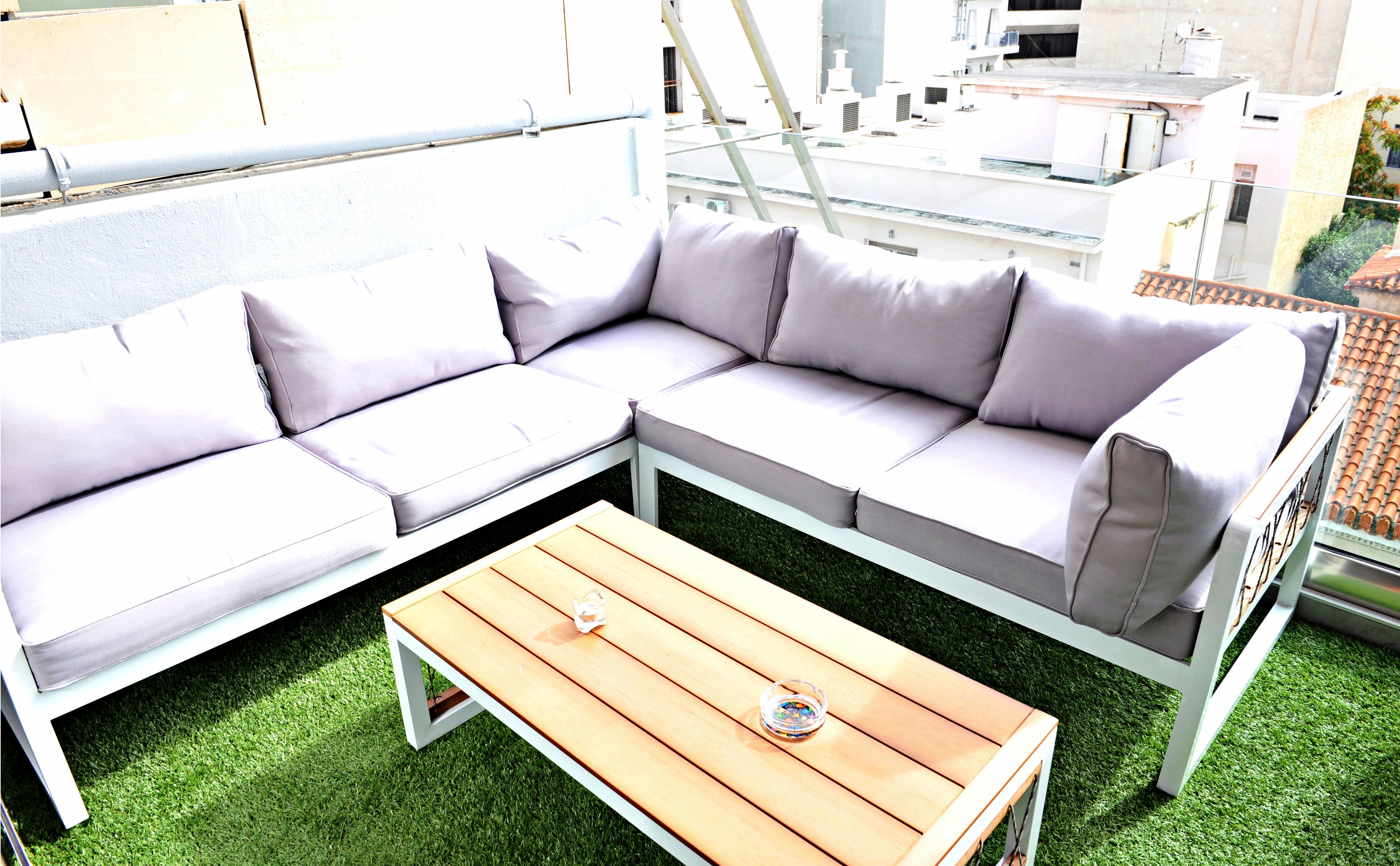 Un canapé modulable et une table en bois sur une terrasse sur le toit, recouverte de gazon synthétique.