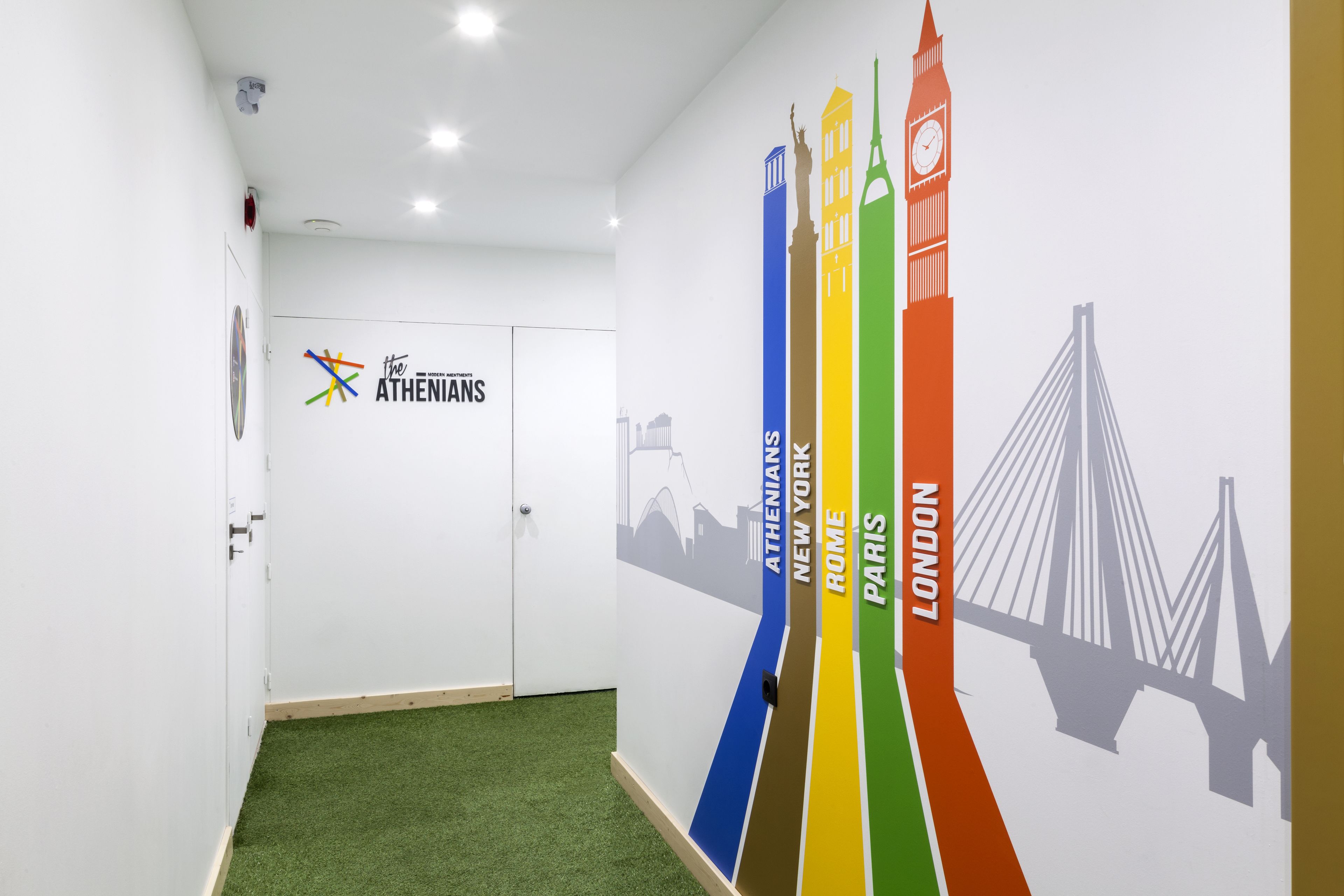 A hallway with a green carpet, white walls, and a logo for 'The Athenians'.