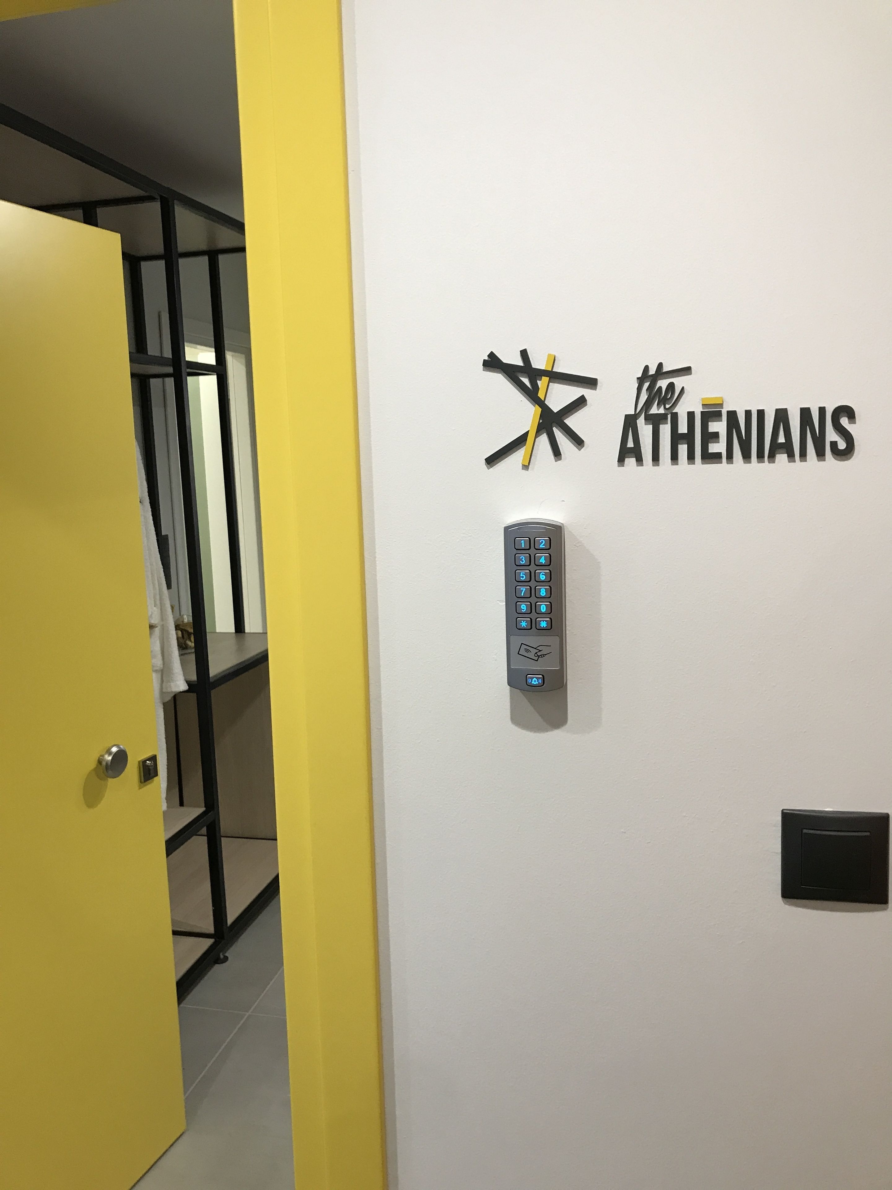 Un clavier fixé au mur et une plaque portant l’inscription « LES ATHÉNIENS », avec un motif de croix stylisé.