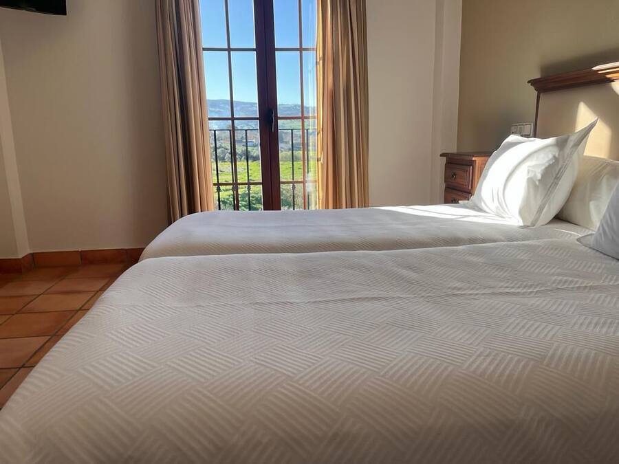 Un dormitorio con dos camas, un ventanal con cortinas y vistas al exterior.