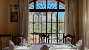 Mesa de comedor preparada para seis personas, con vista a un paisaje montañoso a través de un amplio ventanal con barrotes de metal.
