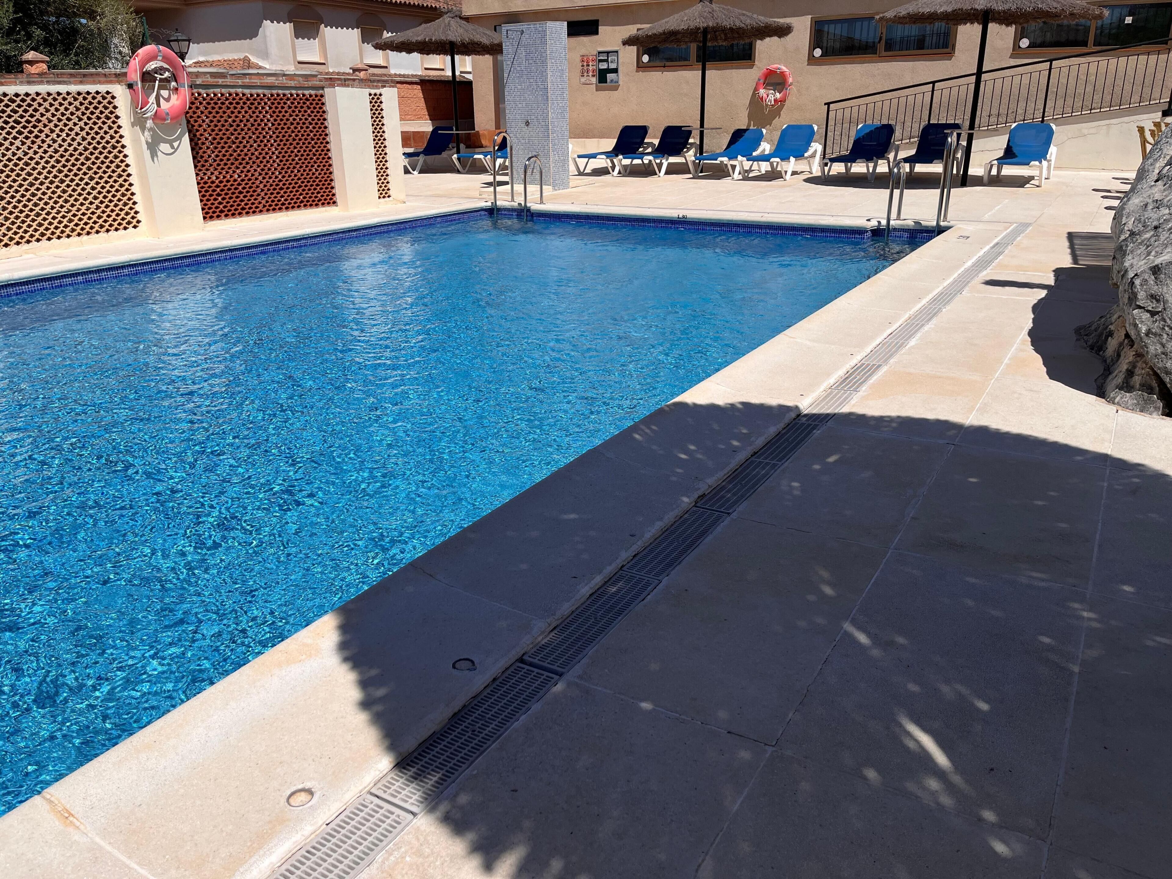 A swimming pool with clear blue water, surrounded by lounge chairs and a lifebuoy.