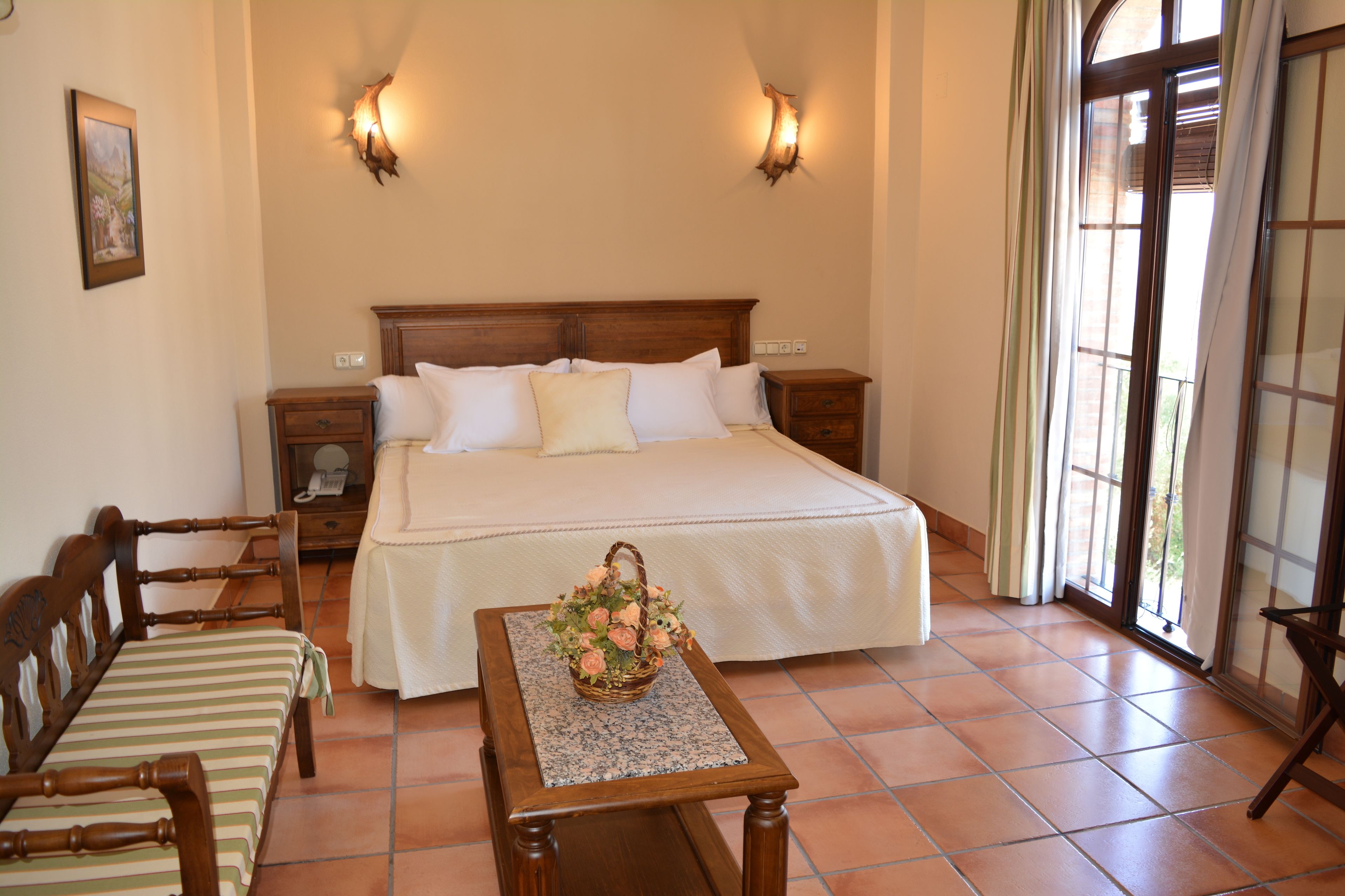 A neatly arranged bedroom with a large bed, a wooden nightstand, a chair, and a small table with a flower basket.