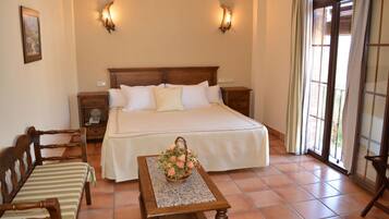 A neatly arranged bedroom with a large bed, a wooden nightstand, a chair, and a small table with a flower basket.