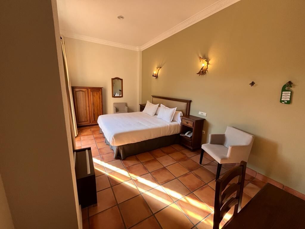 A hotel room with a large bed, bedside tables, a chair, and wall-mounted lights.