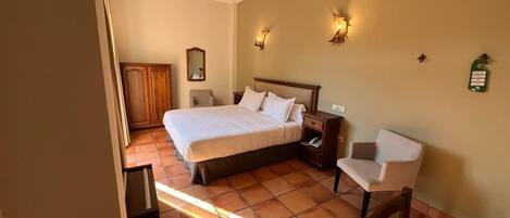 A hotel room with a large bed, bedside tables, a chair, and wall-mounted lights.