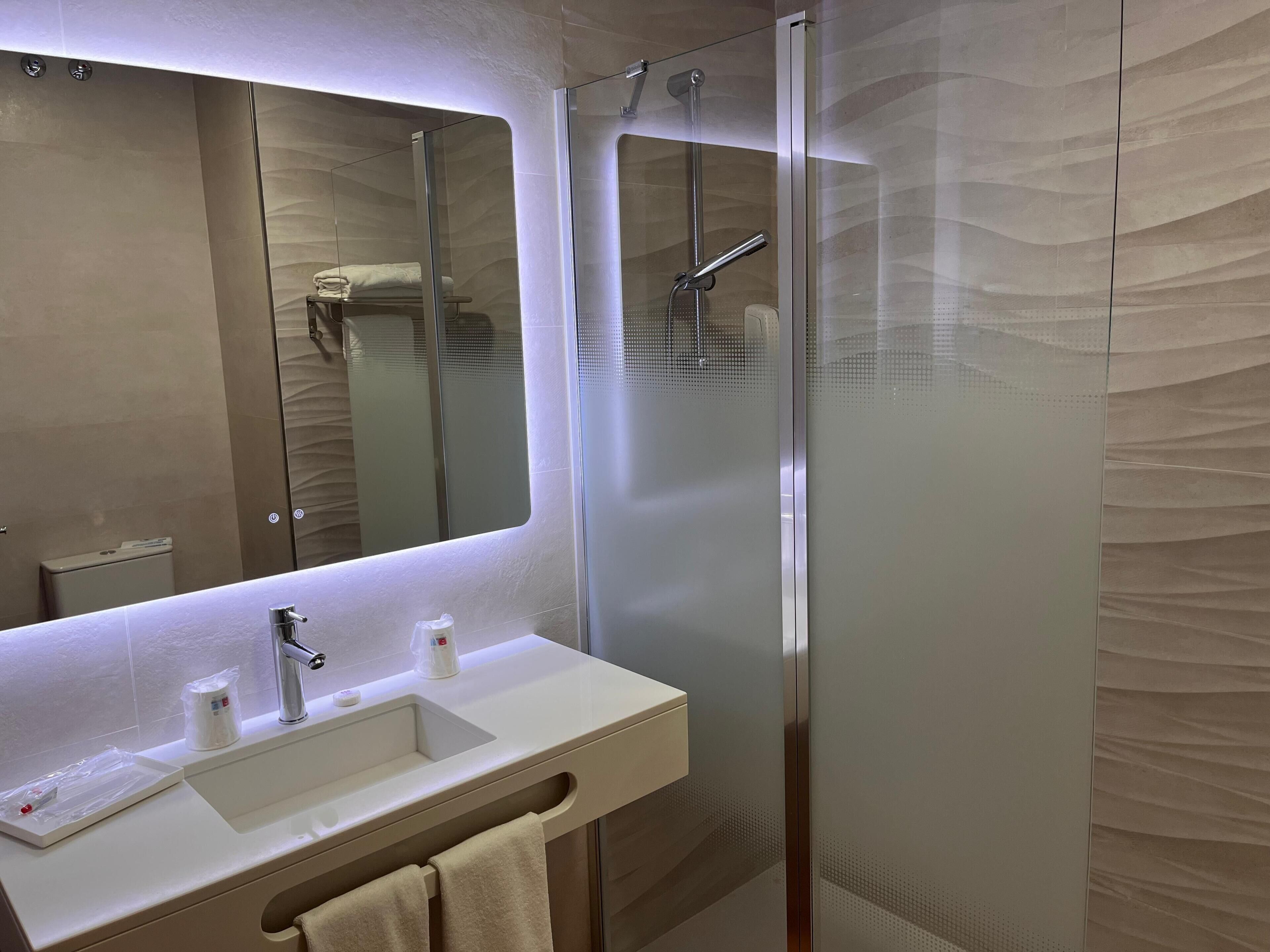 A modern bathroom with a glass shower enclosure, a sink with a mirror above it, and a towel rack.