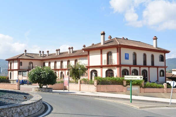 Un edificio de dos pisos con fachada roja y blanca, varios chimeneas y un letrero que indica 'urbanización'.
