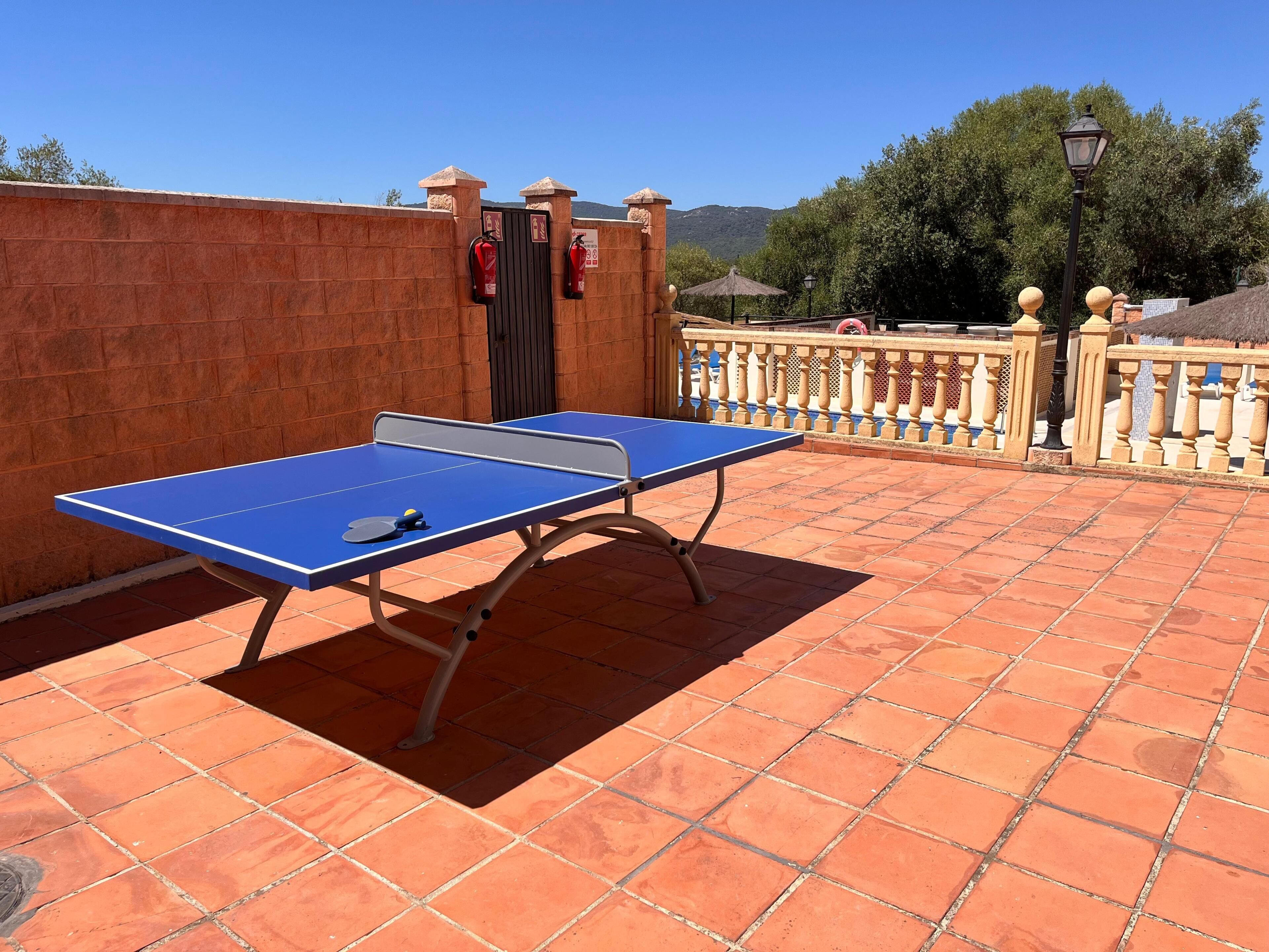Una mesa de ping pong en un patio con baldosas, una pared de ladrillo y una barandilla metálica.