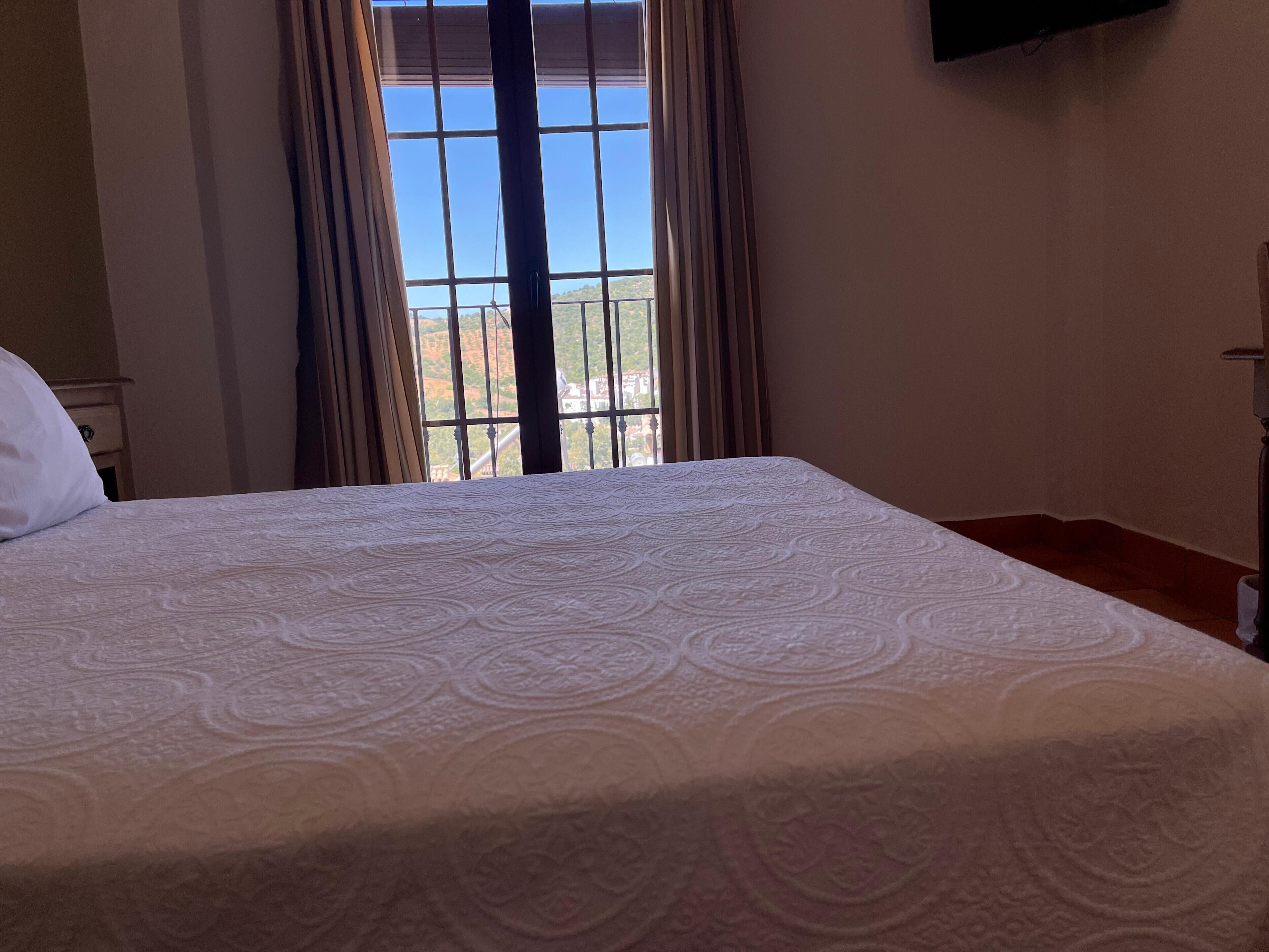 A hotel room with a large bed, a window with curtains, and a television mounted on the wall.