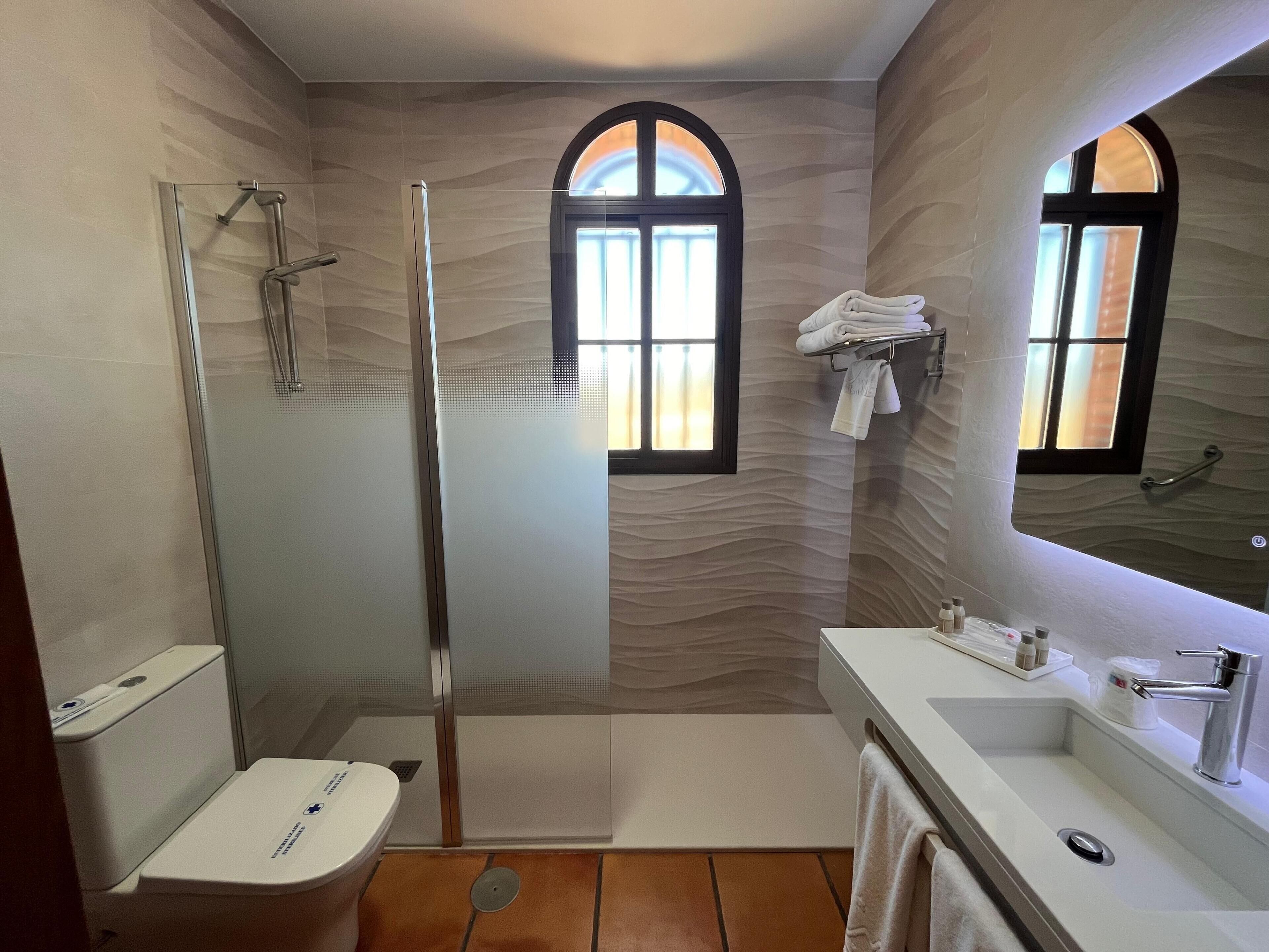 Un baño con ducha envuelta en vidrio, inodoro, lavamanos con espejo y toallero.
