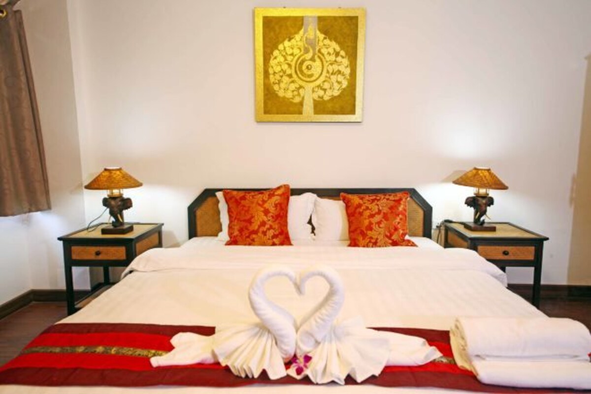 A hotel room with a bed, two nightstands, lamps, a decorative wall piece, and a heart-shaped towel arrangement.