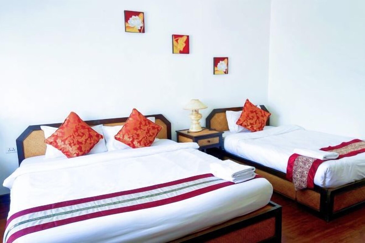 A hotel room with two beds, each with white bedding and red pillows. There are small paintings on the wall and a lamp on the nightstand.