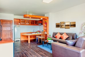 A modern kitchen with wooden cabinets, a dining table, and a sofa in the living area.