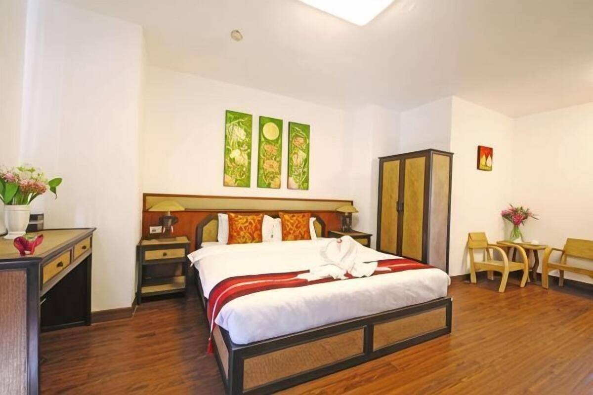 A hotel room with a bed, bedside tables, a desk, a chair, a wardrobe, and a small table with flowers.