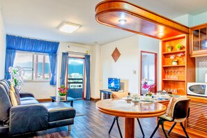 A living room with a sofa, a dining table, a TV, and a view of the city. - Jade Tower Downtown (Chiang Mai)