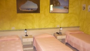 A room with three single beds, each with a bedside table and lamp. The walls are yellow, and there are two framed pictures depicting coastal scenes. - Rosa Hotel (Capoterra)