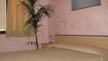 A bedroom with a bed, a nightstand, a lamp, and a potted plant.