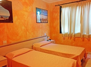 Una habitación de hotel con dos camas, un televisor en la pared y una ventana con cortinas.
