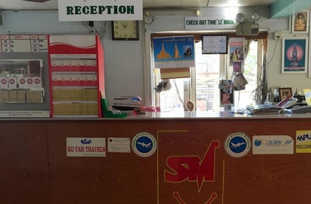 A reception desk with a clock, a sign for check-out time, and various travel-related stickers.