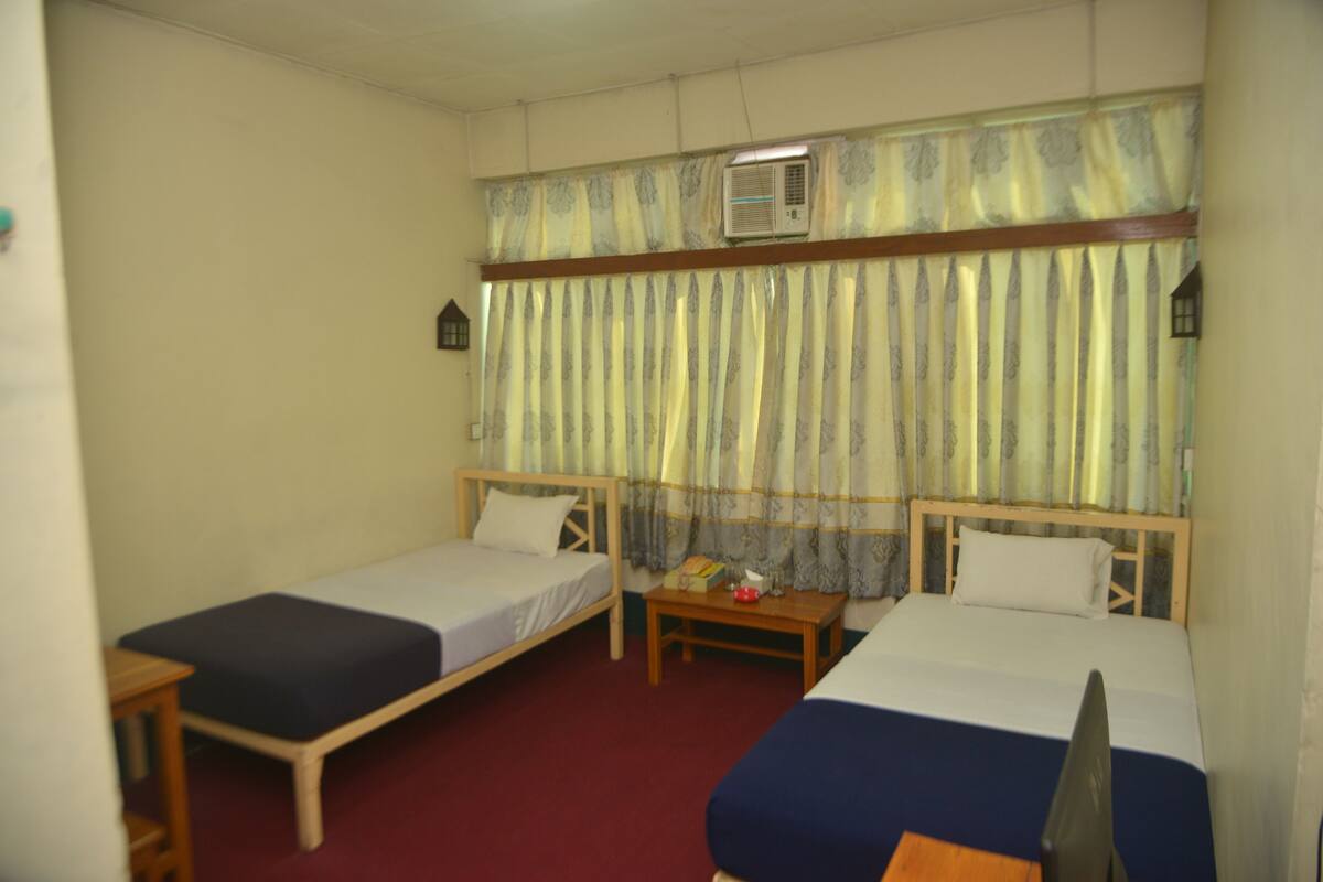 A room with two single beds, a small table, and an air conditioning unit.
