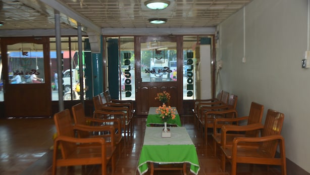 Un comedor con sillas de madera y una mesa cubierta con mantel verde, con un jarrón de flores.