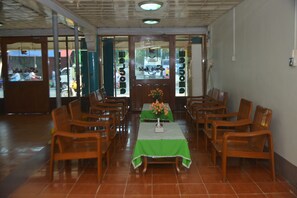 A dining area with wooden chairs and a table covered with a green tablecloth, featuring a vase of flowers.