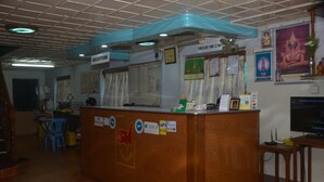 Un mostrador de recepción con detalles de madera, un reloj y varios carteles, incluyendo un aviso con la hora de salida.