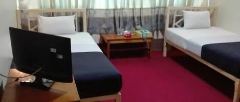 Une chambre avec deux lits, un bureau avec un ordinateur portable, une petite table et une fenêtre avec des rideaux.