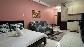 A modern hotel room with a bed, a sofa, a painting, a kitchen area, and a tiled floor. - Manila Lee - Malate Bayview Mansion (Manila)