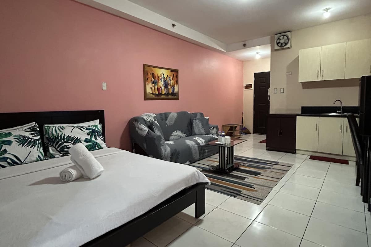 Una habitación de hotel moderna con cama, sofá, un cuadro, una zona de cocina y suelo de baldosas.