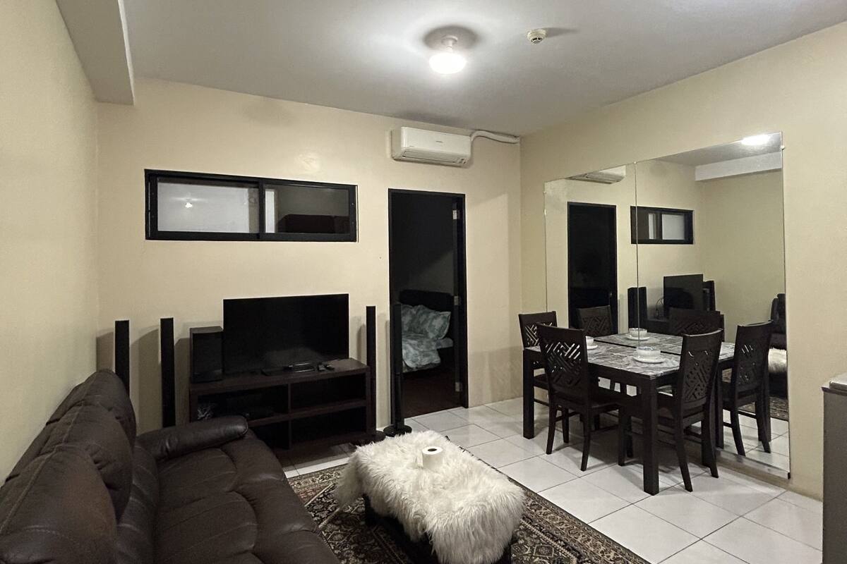 Una sala de estar con un sofá marrón, un televisor y un comedor con una mesa y sillas.