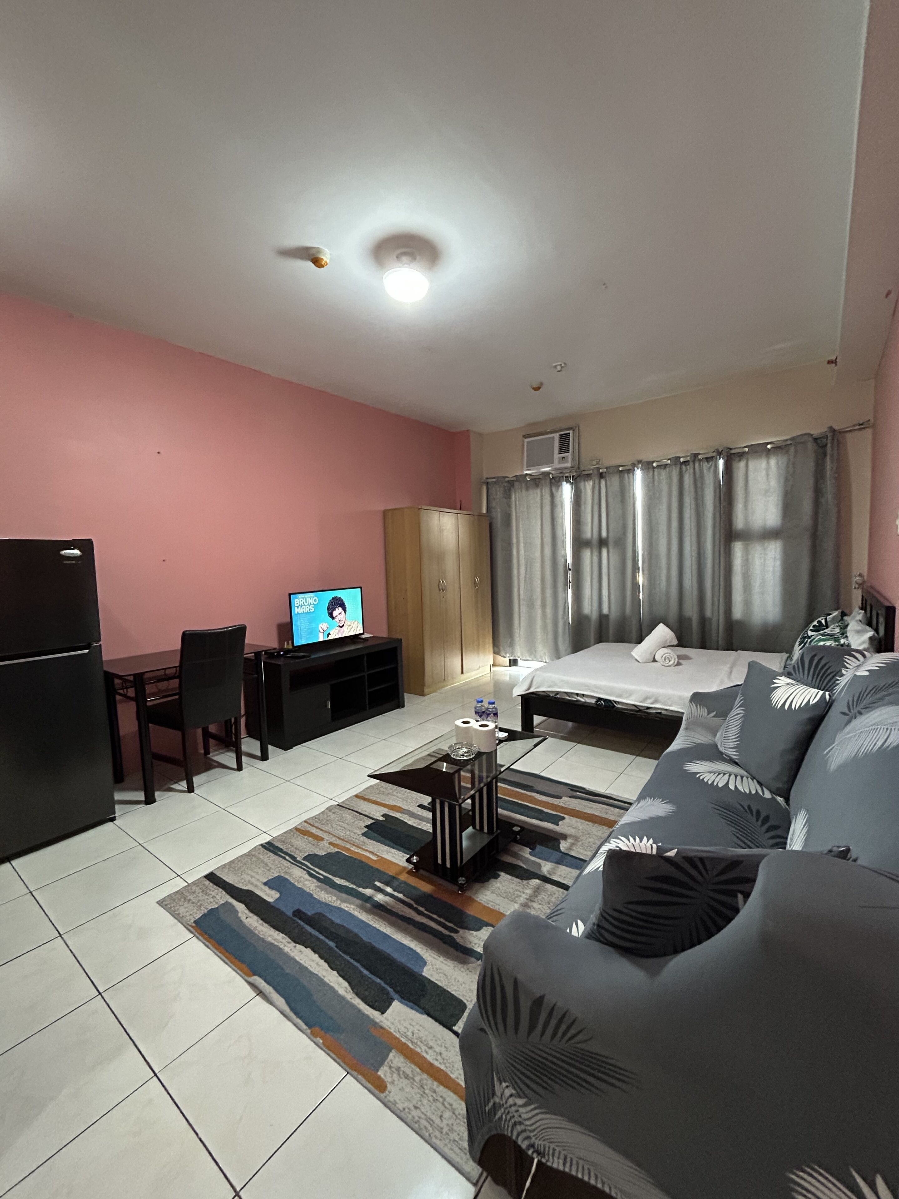 A hotel room with a bed, a sofa, a desk with a television, a refrigerator, and a patterned rug.