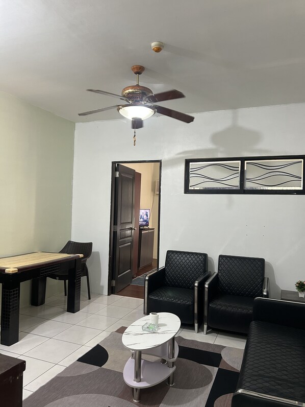 A living room with a ceiling fan, a dining table with chairs, a small coffee table, and two black armchairs.