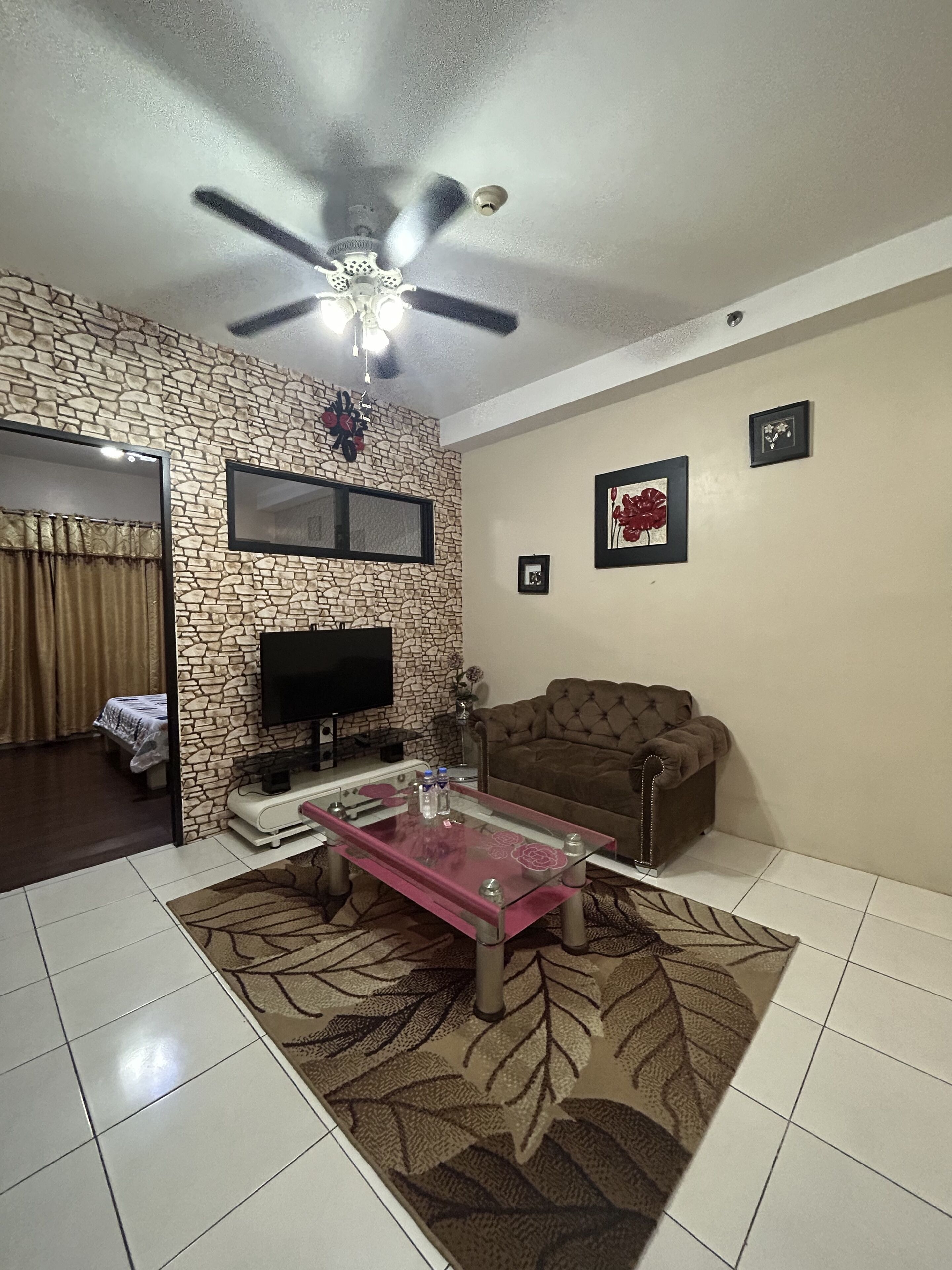 A living room with a stone wall, a ceiling fan, a flat-screen TV, a brown sofa, and a glass coffee table.