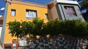 Ein zweistöckiges Gebäude mit gelber Fassade, Steinwand und einem kleinen Garten.