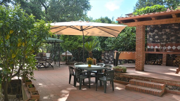 Eine Terrassengruppe mit Tisch und Stühlen, umgeben von Kübelpflanzen und einem Grillbereich mit Backsteinofen.
