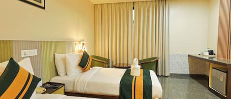 A hotel room with two beds, a desk, a chair, a minibar, and a large window with curtains.