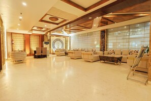 A spacious lobby with a high ceiling, a central seating area with sofas and chairs, and a large window providing natural light. - Hotel Silk City (Varanasi)