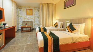 A hotel room with two beds, a desk, a television, and a ceiling fan. - Hotel Silk City (Varanasi)
